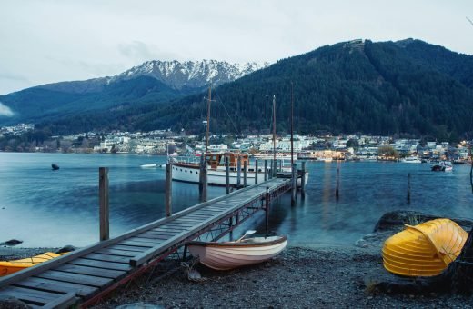 Picturesque view of Queenstown harbor with boats, dock, and mountains.